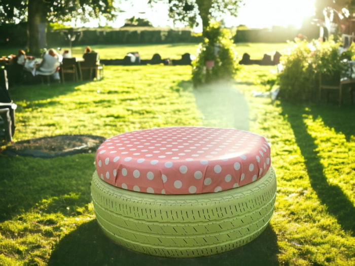 Un tabouret fabriqué à partir d'un vieux pneu peint en vert et recouvert d'un tissu à pois roses, lors d'une fête ensoleillée dans l'arrière-cour.