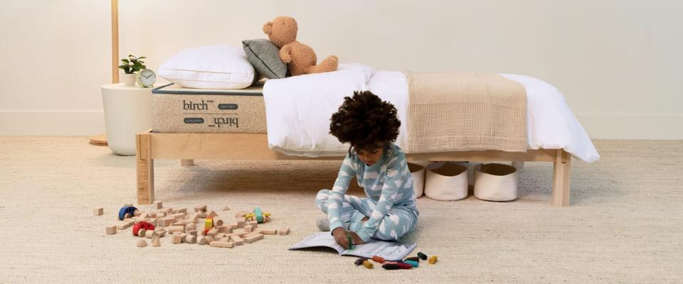 Child colors on the floor in front of a bed with the Birch Kids Natural Mattress