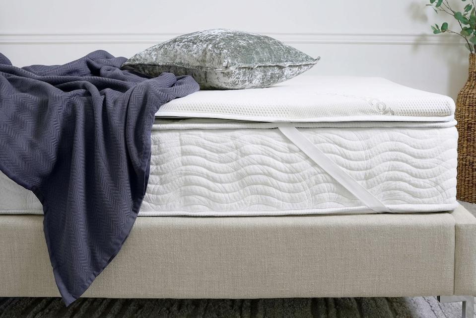 The Saatva Graphite Memory Foam Mattrss Topper on a mattress with a blanket and pillow on it