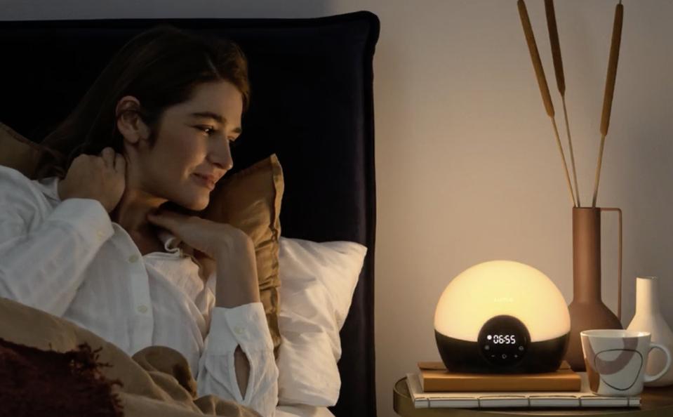 Lumie Bodyclock Glow 150 on a bedside table with a person next to it. 