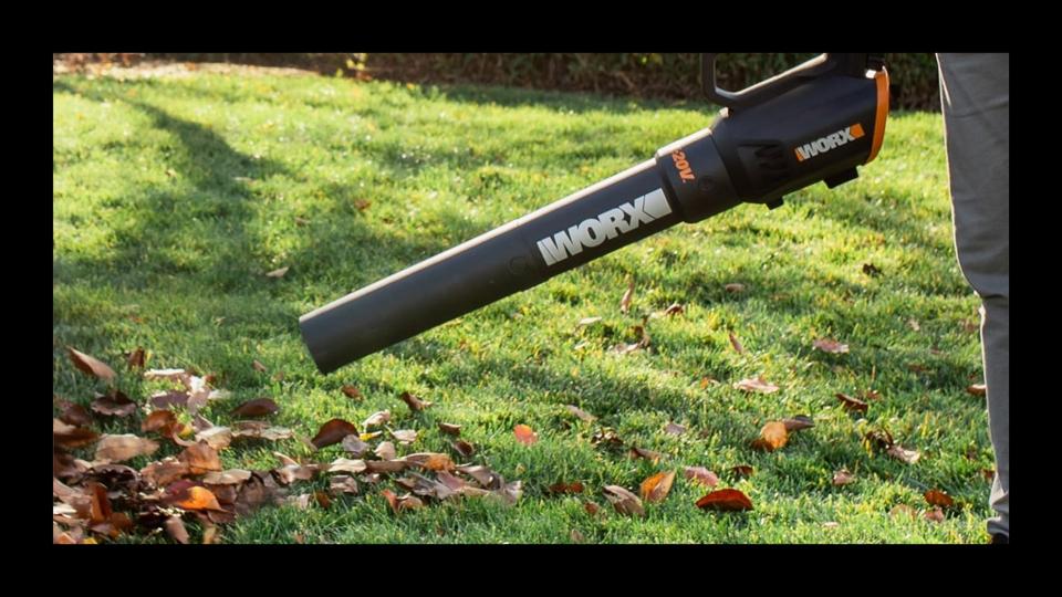 A Worx 20V Turbine Cordless Two-Speed Leaf Blower blowing around leaves in a yard. 