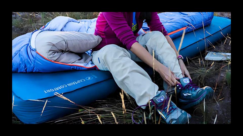 A woman tying her hiking shoes while sitting on a camping air mattress