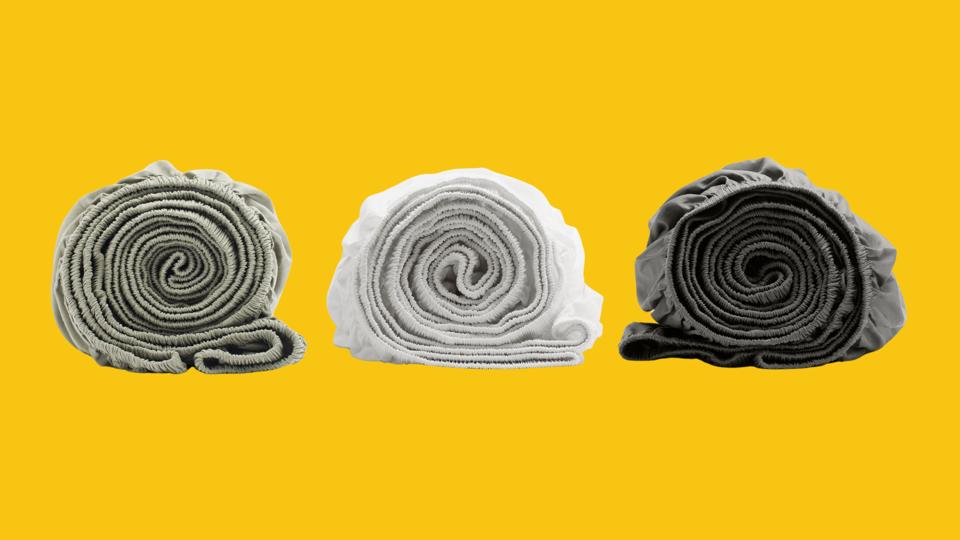 Three Boll & Branch fitted sheets in different colors rolled up on a yellow background