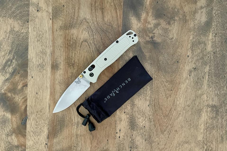 A Benchmade Bugout pocket knife in grey next to a soft pouch case on a wooden background