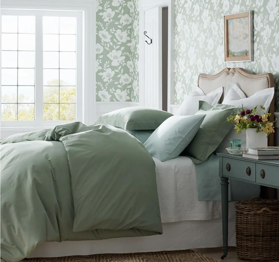 The Company Store Percale Sheets in green on a bed in a green floral wallpapered room. 