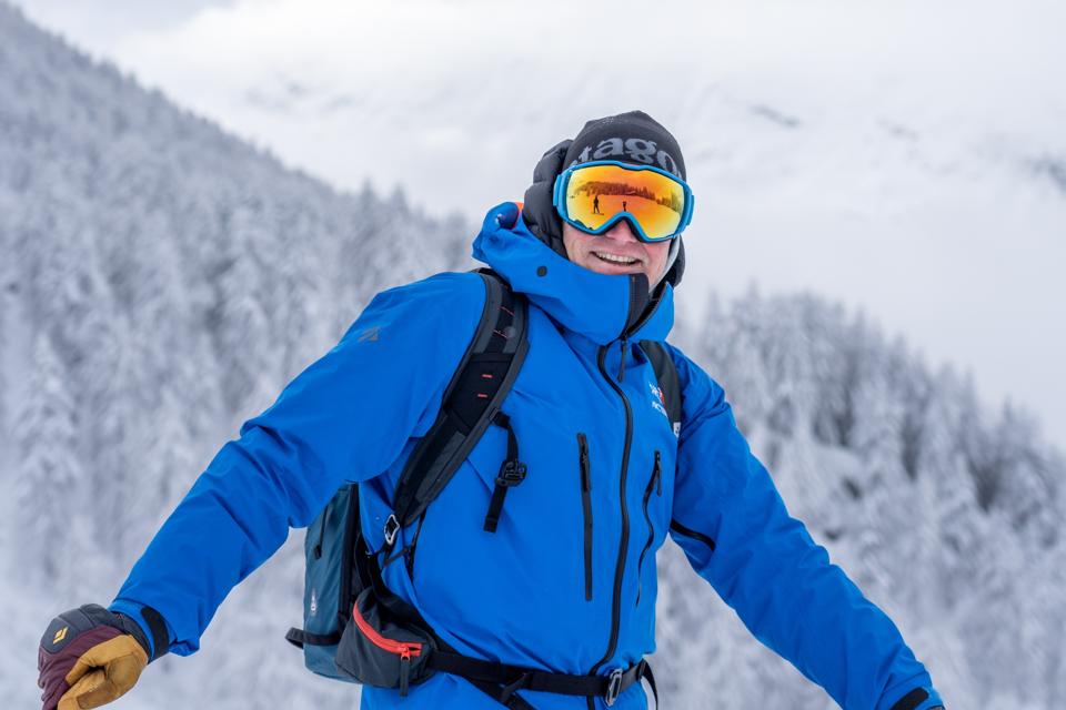 A man smiling while wearing a blue winter coat and ski goggles