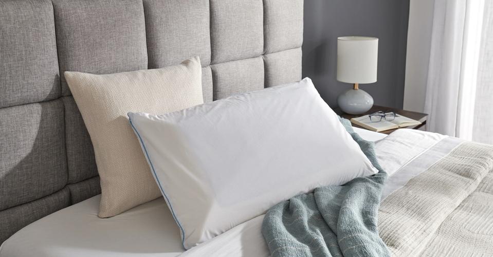 The Temper-Cloud Dual Breeze pillow on a bed with a thin blanket and another pillow. 