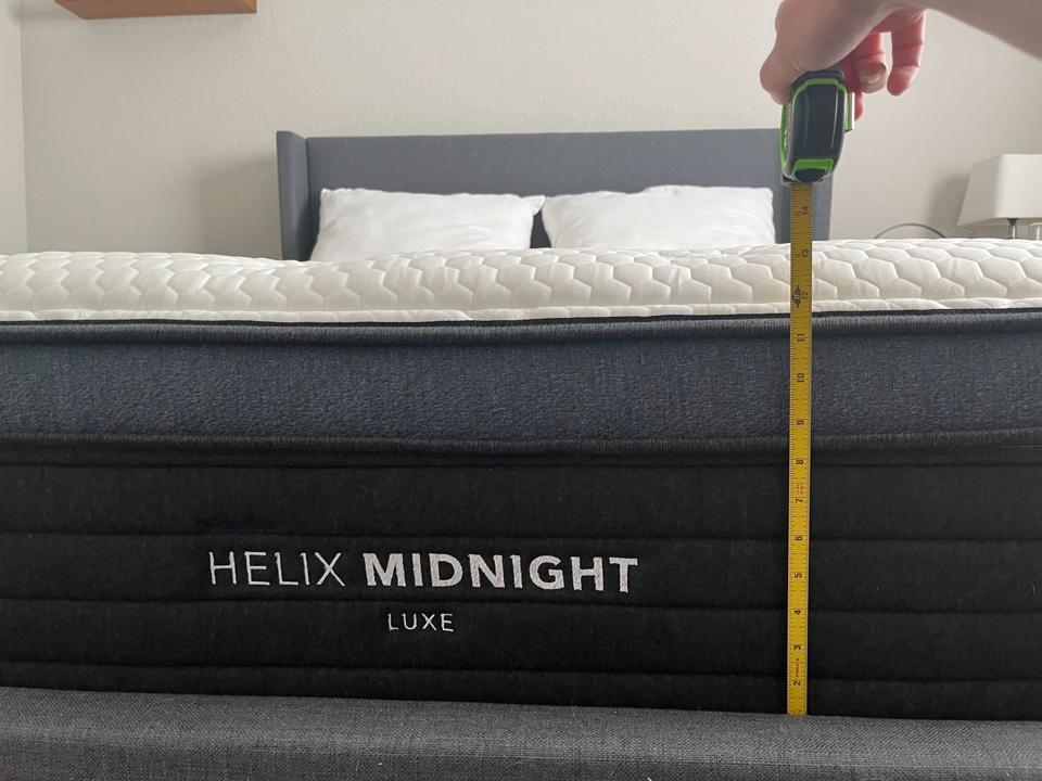 A hand using a tape measure in front of the Helix Midnight Luxe to show its height