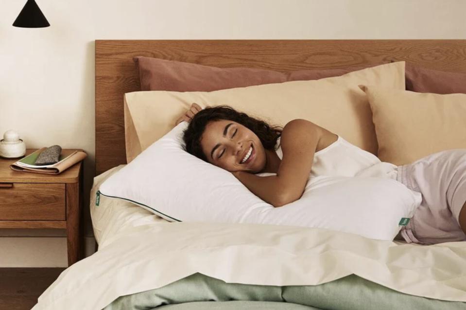 A woman lying on a bed with the Brooklinen Marlow Pillow