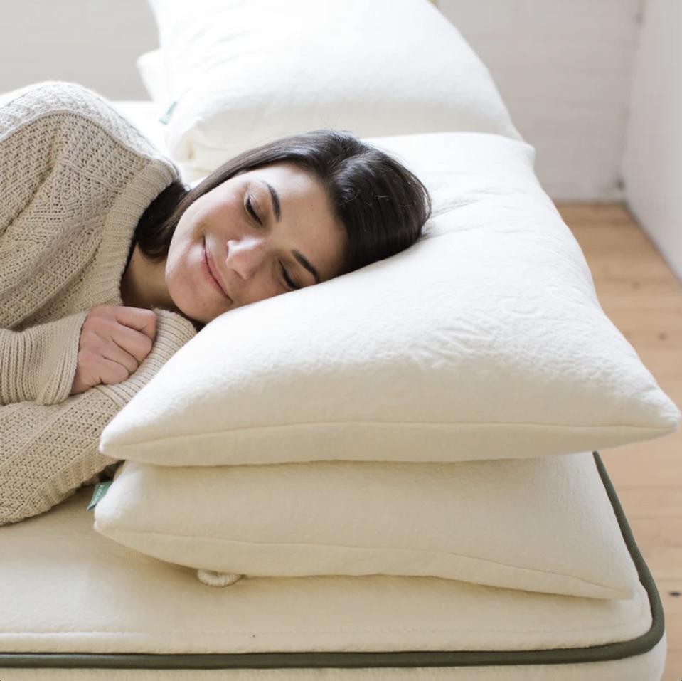 Woman lying on her side against two Avocado Green Pillows on bed in bright room.