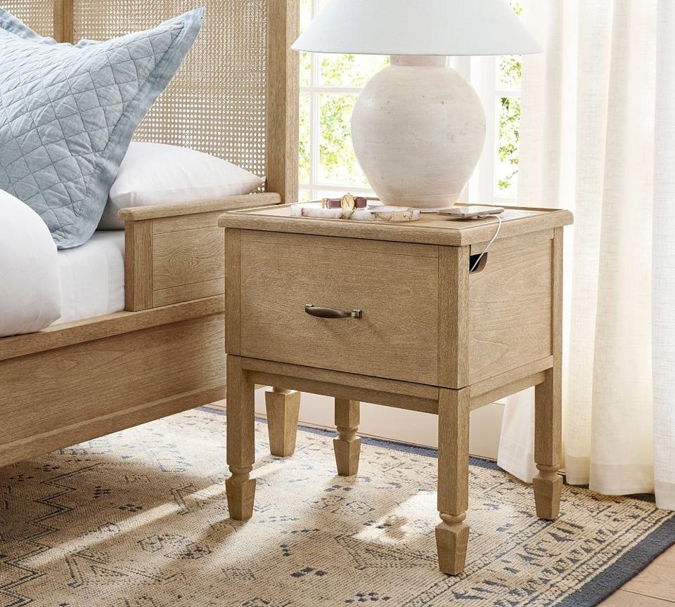 A light brown nightstand with cords coming out a cutout holds a CPAP machine.