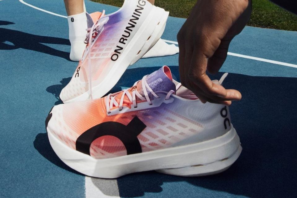 A person holding the On Cloudboom Strike racing shoes on a blue track