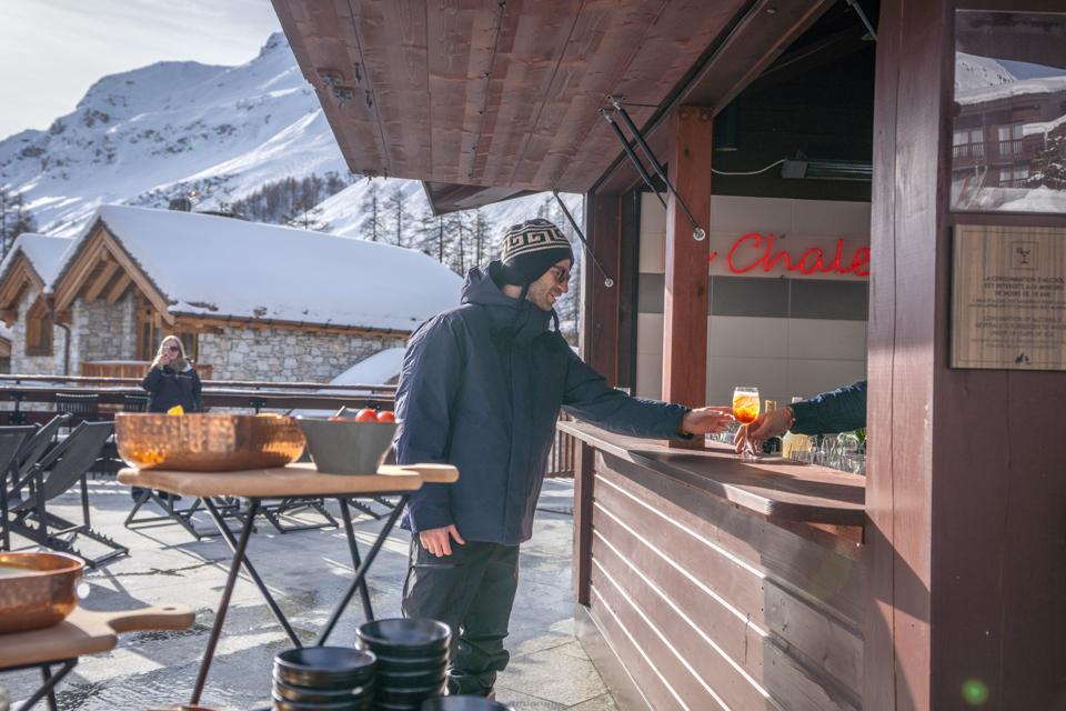 A man reaching for a drink on a patio in winter attire at a ski resort