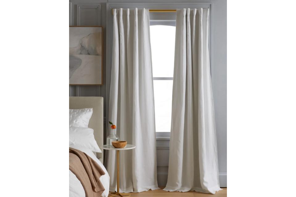 Quince European Linen Blackout Curtain in white hanging on a bright window by a bed