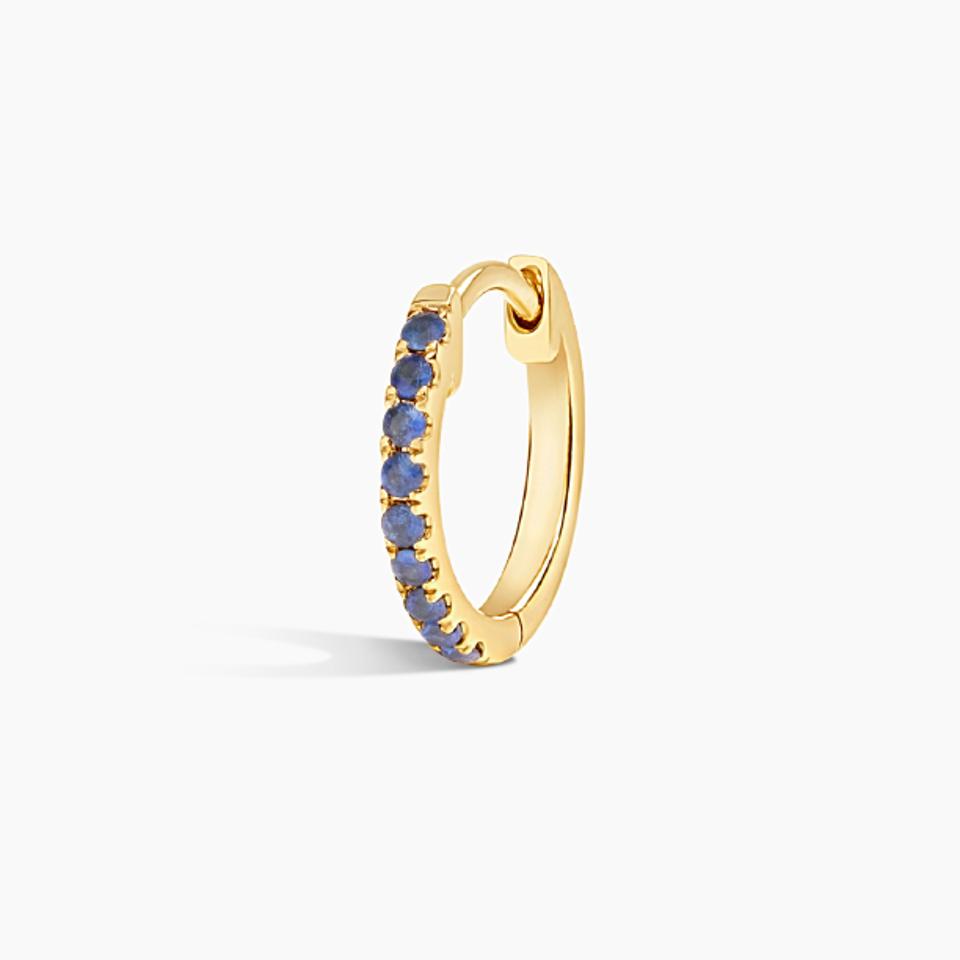 A single golden hoop earring with sapphires inlaid throughout the front-facing edge.