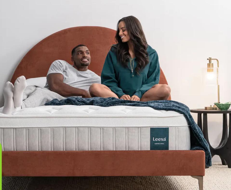 A couple on the Leesa Sapira Chill Hybrid Mattress on a bed frame next to a nighstand.