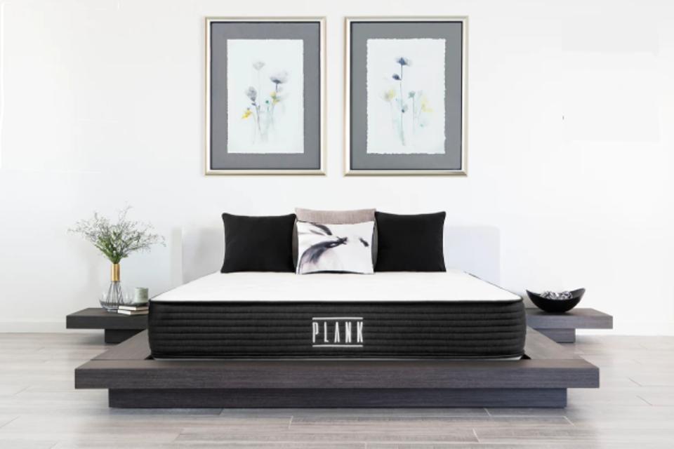 Plank Firm mattress in white room on modern gray platform bed frame with two pictures above.