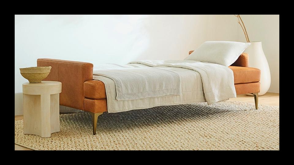 West Elm Andes Leather Futon w/ sheets & pillow on beige carpet in minimal living room