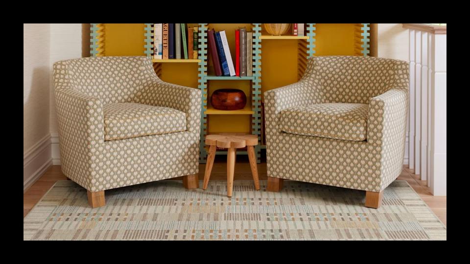 The Ruggable Architectural Digest Selene Neutral Multicolor Tufted Rug placed on a floor with two armchairs and a bookshelf