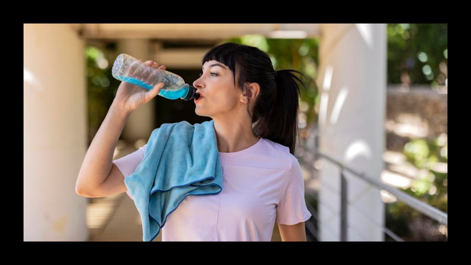 A young woman drinking from a bottle with a cooling towel draped over her shoulder.