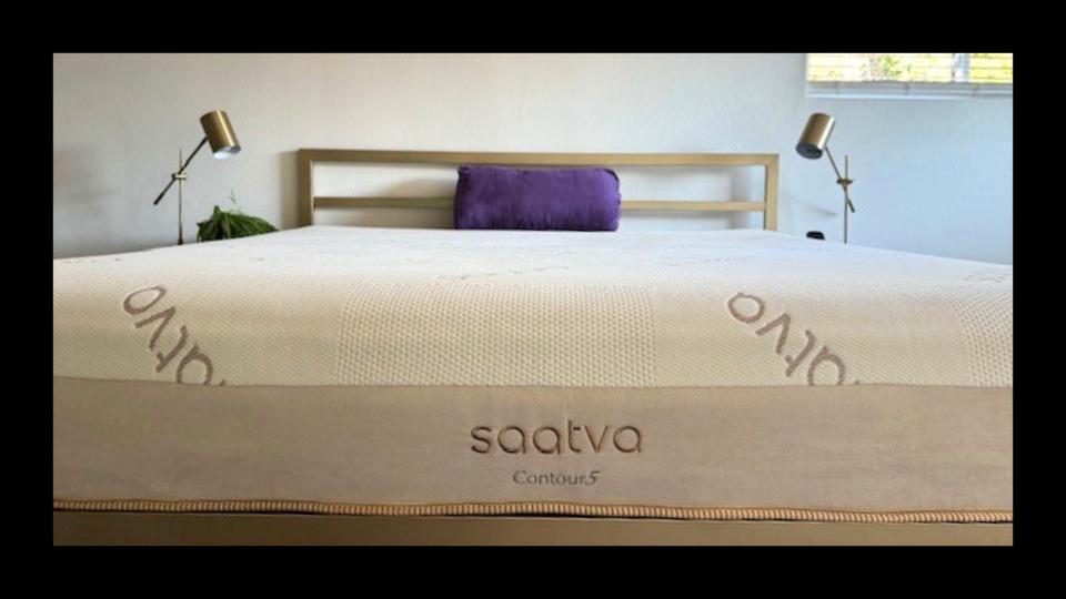 The Saatva Contour5 Mattress on the author's bed frame with a small purple pillow on the mattress.