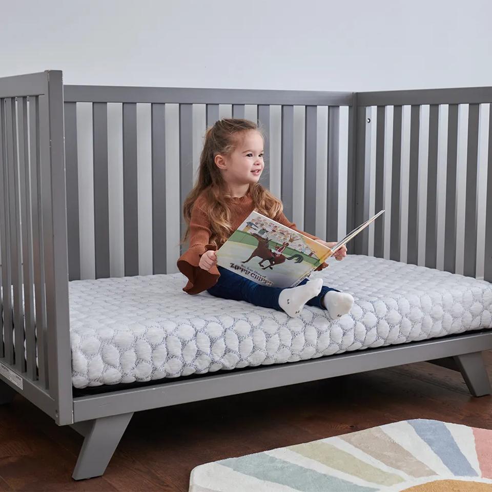 Little girl sits on a toddler bed with the Lullaby Earth 2-stage mattress