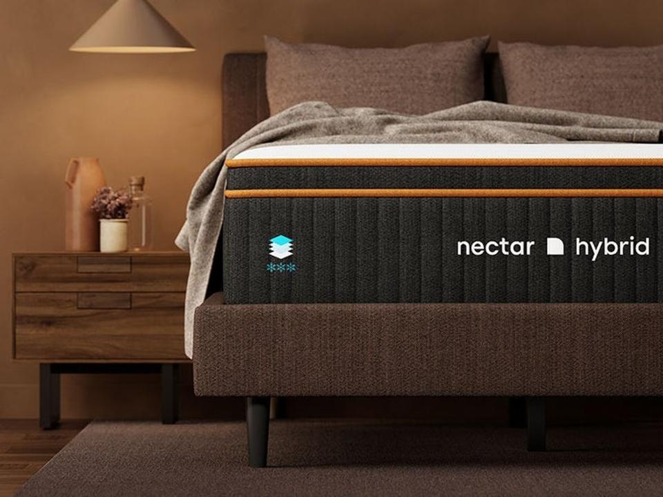 The foot of Nectar's Premier Copper Hybrid Mattress in a dimly lit room topped with blankets and pillows. 