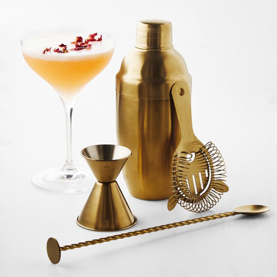 Williams Sonoma Classic Bar Tools Set in Antique Brass next to a cocktail.