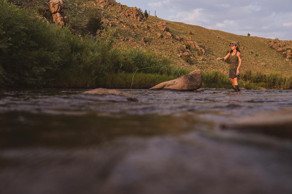 A woman fly fishes in a stream.