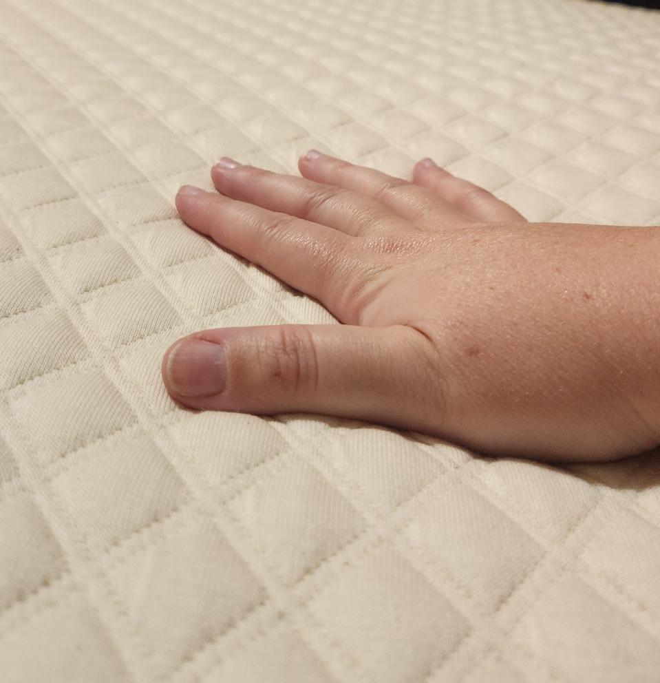 A woman's hand touching the top of the Nolah Luxury Firm Mattress Topper.