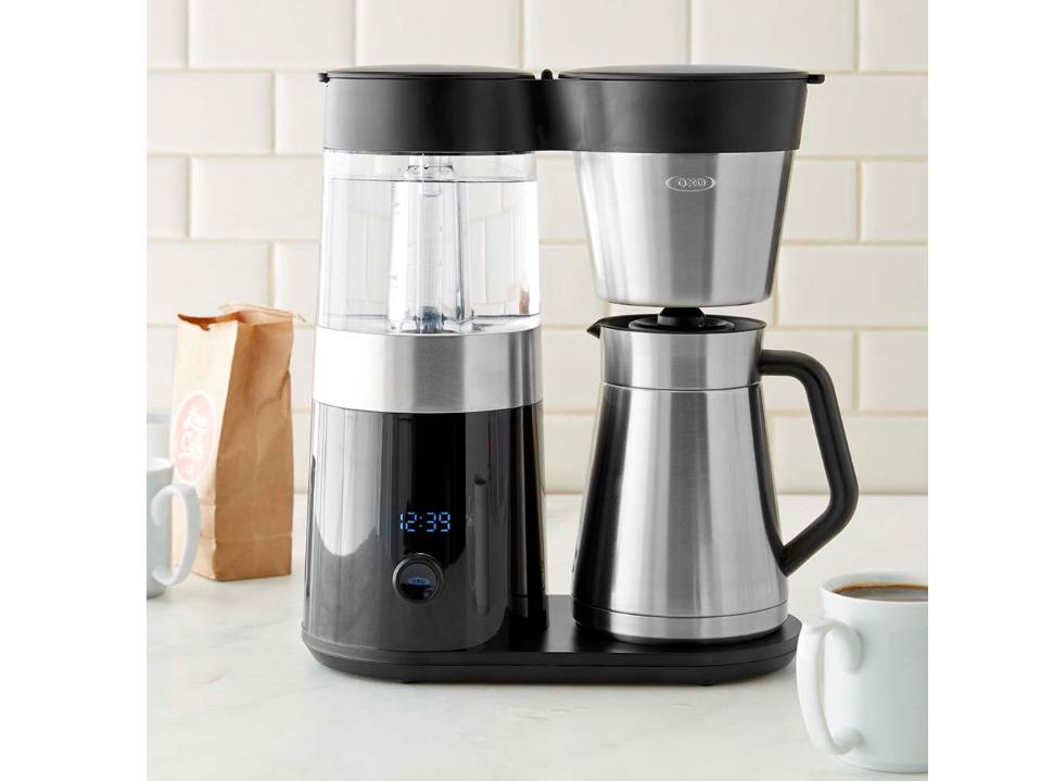 image of OXO Brew 9 Cup Stainless Steel Coffee Maker on white kitchen counter next to cup