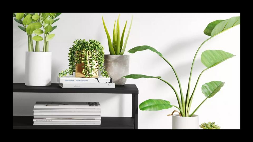 Fake plants in white planters placed on a black sideboard. 