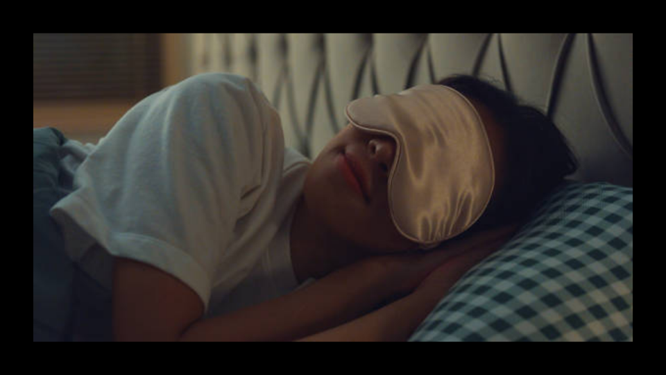 A woman sleeping with a sleep mask on against a black border