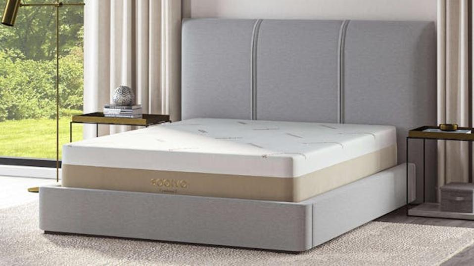 The Saatva Contour5 mattress on a light grey bed frame in a brightly lit bedroom.