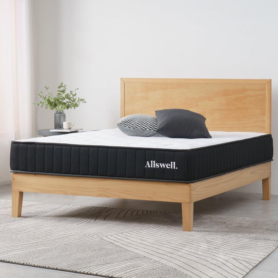 The Allswell 10" Hybrid Mattress on top of a wooden bed frame inside a bright bedroom. 