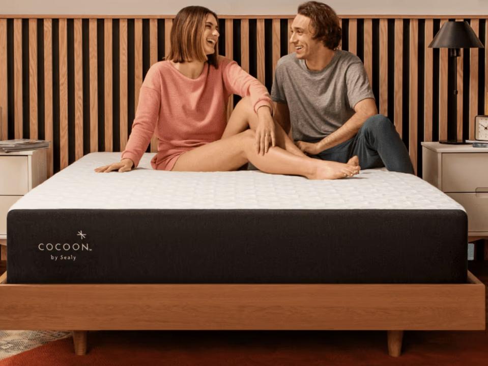 The Cocoon Chill mattress on a wooden bed frame with two people on top. 