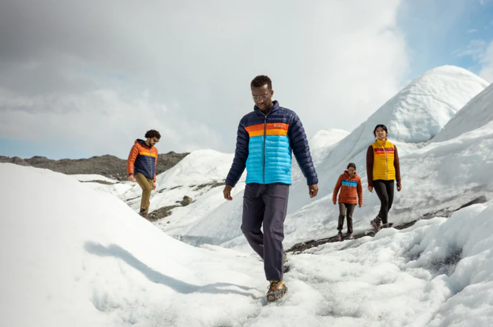 Four people wearing colorful Cotopaxu jackets while hiking in the snowy mountains