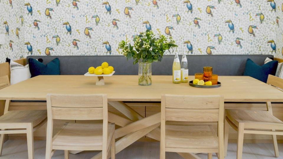 A wooden kitchen table with a navy banquette and bird wallpaper.