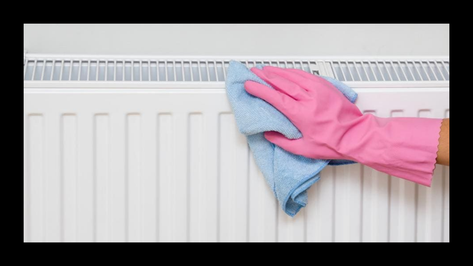 A hand in a pink glove cleaning a radiator with a microfiber cloth.