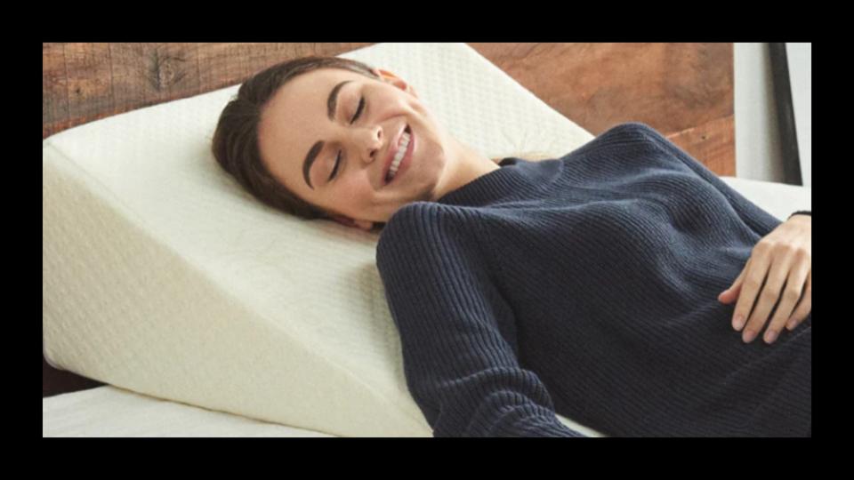 A woman lying on her back on the Brentwood Home Wedge Pillow with a black border