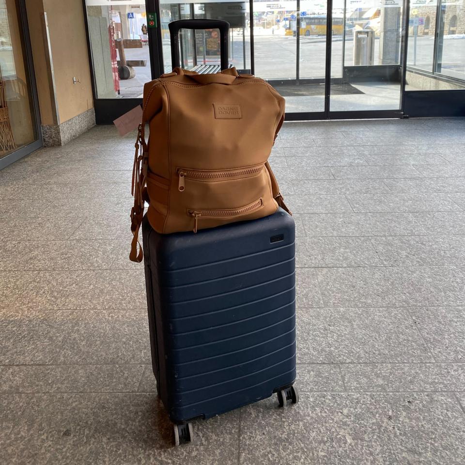 A dark blue suitcase with a brown bag sitting on top of it.