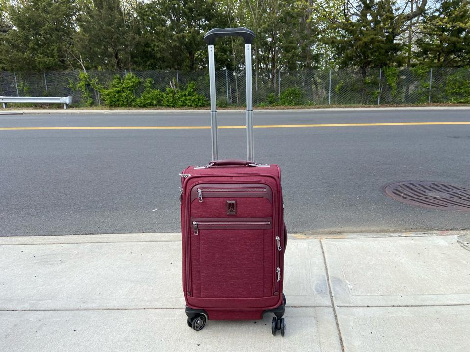 A burgundy suitcase on a street.