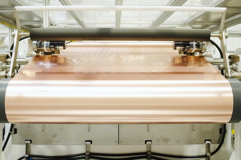 A large industrial machine rolls up a spool of copper