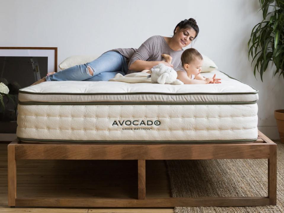 The Avocado Green Mattress in a beige room with a parent and baby on it. 