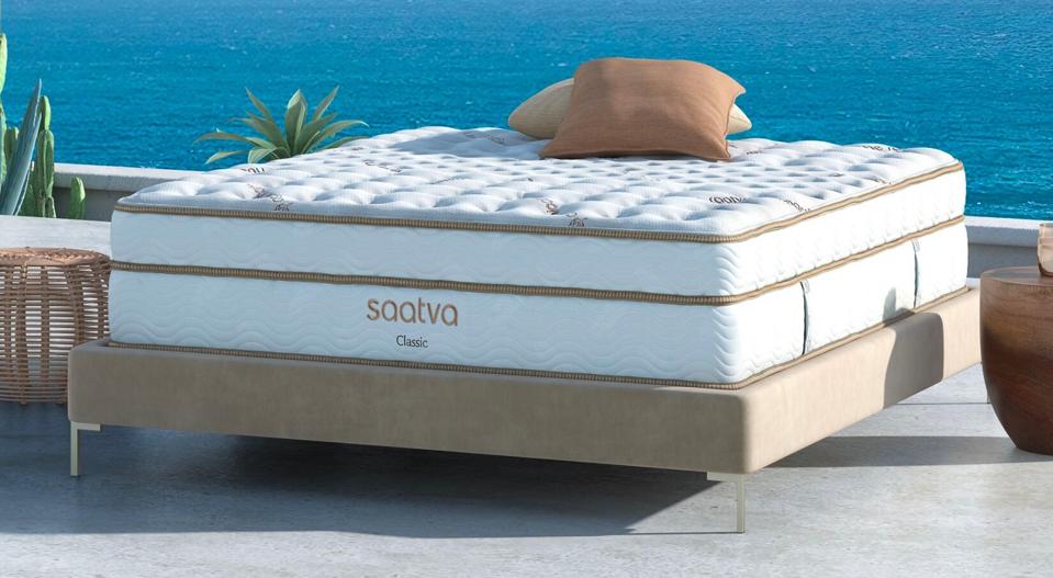 The Saatva Classic mattress on a tan bed frame with an ocean in the background. 