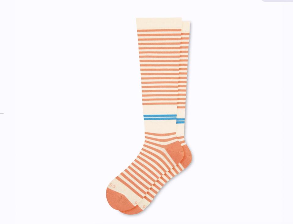 Cream colored compression socks with orange and blue stripes on a grey background