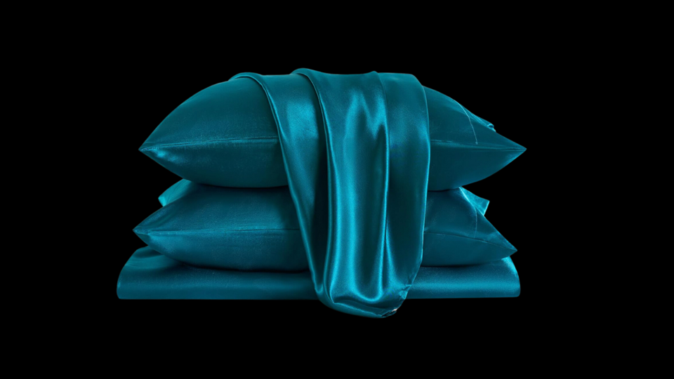 A set of folded satin sheets in deep teal on a black background