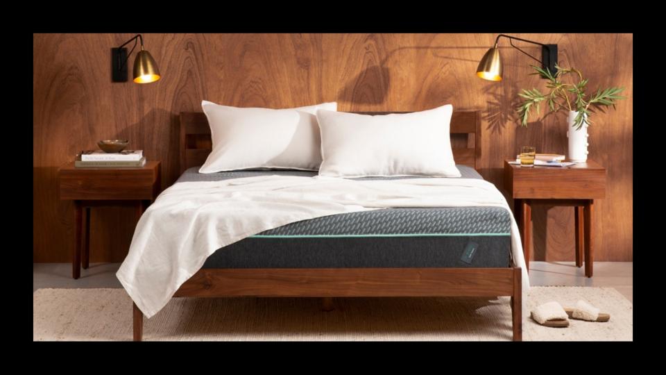 The Tuft & Needle Mint Hybrid Mattress on a low wood bed frame with a blanket and pillows