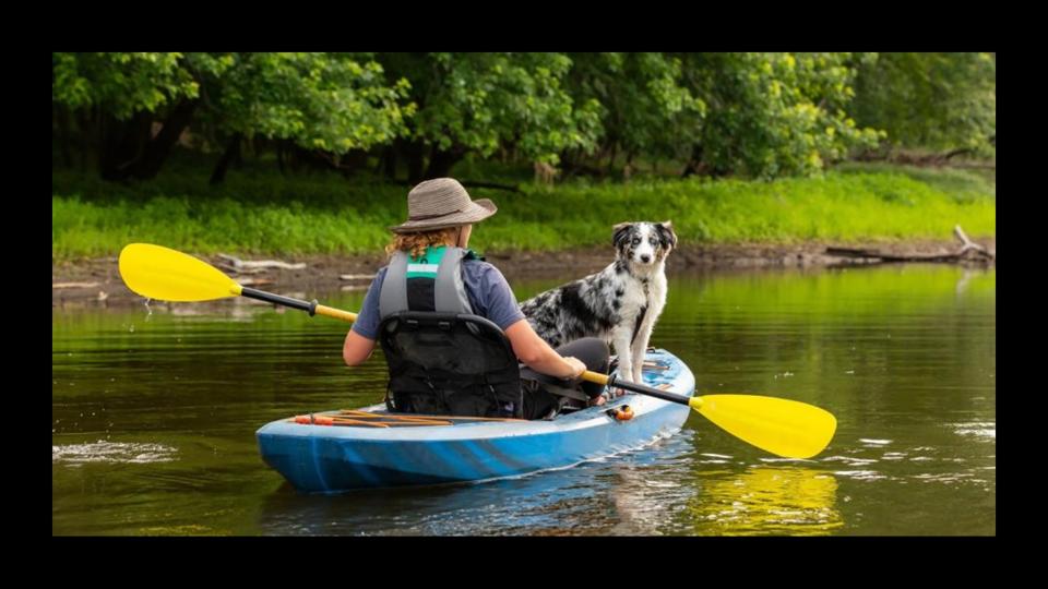 A woman wearing a hat while kayaking with her dog.