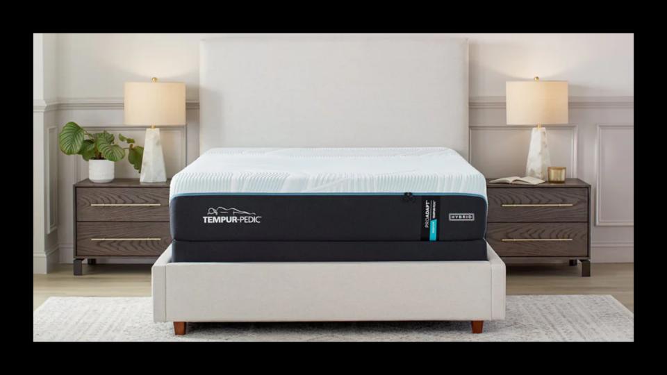 The Tempur-Pedic ProAdapt Medium Hybrid mattress on a light grey bed frame in between two nightstands with lamps on top.